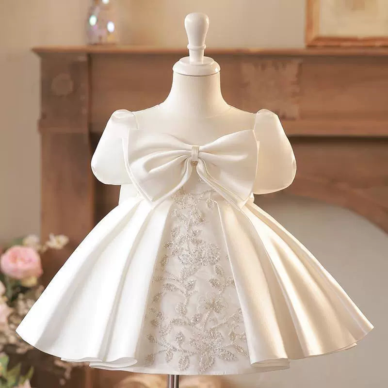Un incantevole abito da principessa, perfetto per rendere magico ogni momento speciale della tua bambina! Realizzato in satin di alta qualità, presenta una gonna voluminosa con meravigliose pieghe verticali, creando un effetto regale e raffinato.

Sul davanti, al centro, spicca un splendido applicazione di perline e paillettes a forma di fiore, che dona un tocco di luce e raffinatezza. La parte superiore è impreziosita da un'ampia fascia di raso che avvolge delicatamente il petto, esaltando la silhouette co